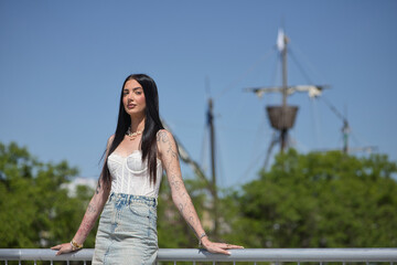 Young woman, brunette, tall, slim and very tattooed, wearing white top and denim skirt, posing...