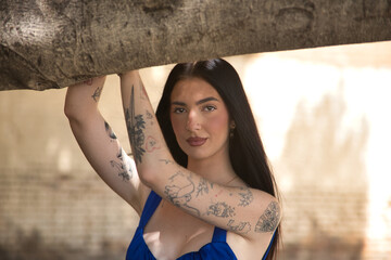 Portrait of a young woman, brunette, tall, slim and very tattooed, wearing a blue top with a sweet...
