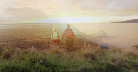 Sun glinting on water spurring senior hiking couple planting pole, walking along dune toward sunset - Powered by Adobe