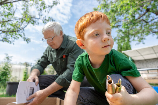 A red-haired boy and his grandfather assembling a trampoline in the garden during spring.