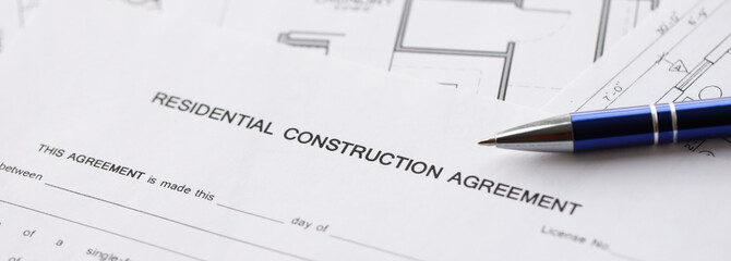 Pen on residential construction agreement and planning blueprints of residential building project...