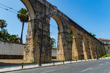 Obraz premium Ancient stone aqueduct with large arches along a cobblestone street under a clear blue sky in Coimbra, Portugal.