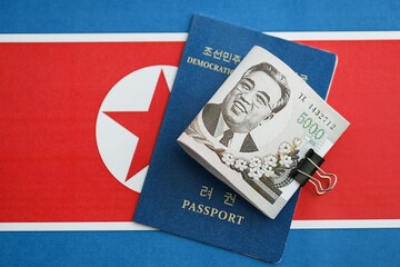 North Korean won money bills in big amount and passport lies on People Republic of Korea flag