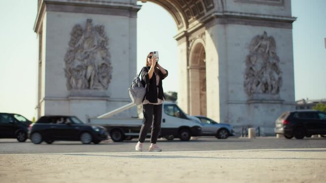 A beautiful woman taking a picture near the Arc de Triomphe in Paris enjoying travel moments and capturing memories during her sightseeing tour of France