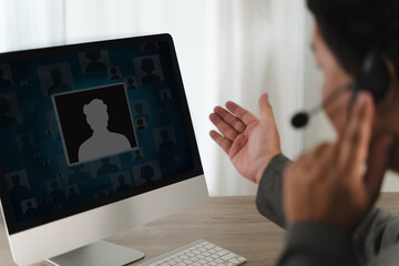 Call center person participating in virtual meeting on computer, wearing headset and gesturing with their hand, in professional setting