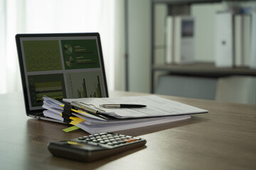 Report file Eco friendly tidy office workspace with documents, pen, calculator, and laptop displaying charts and graphs, suggesting financial