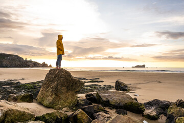 Man standing on rock at sunset beach