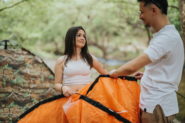 Two friends work together setting up a tent in a scenic outdoor environment. The greenery around...