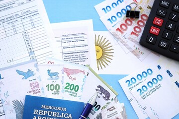 Argentine pesos money bills in big amount lies on table with pen, calculator, passport and tax forms