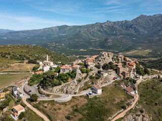 Aerial view of the medieval hilltop village of Sant’Antonino on the Mediterranean island of Corsica with mountains in the distance