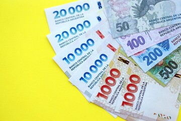 Argentine pesos money bills in big amount lies on yellow color table close up