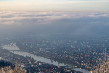 Aerial view of Heidelberg, Germany, with the Neckar River winding through the city beneath a dramatic cloud layer on a cold winter evening.