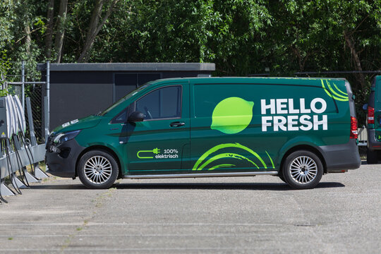 A vibrant green HelloFresh electric delivery van, featuring its logo and "100% elektrisch" text, parked at charging stations, symbolizing sustainable logistics. Utrecht, Netherlands, 15 May 2025.