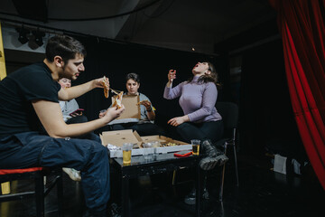 A group of individuals sharing pizza and snacks during a break in a theatrical environment. Friends...