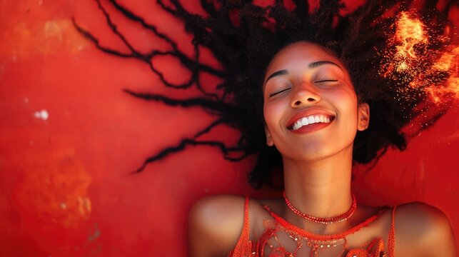 A joyful woman with long, flowing dreadlocks dances against a vibrant orange background.