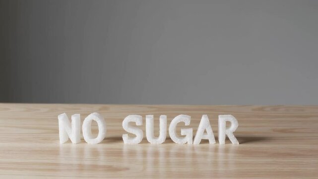 White sugar cubes form the words no sugar on a wooden table against a gray background, creating a paradoxical representation of sugar reduction and healthy choices