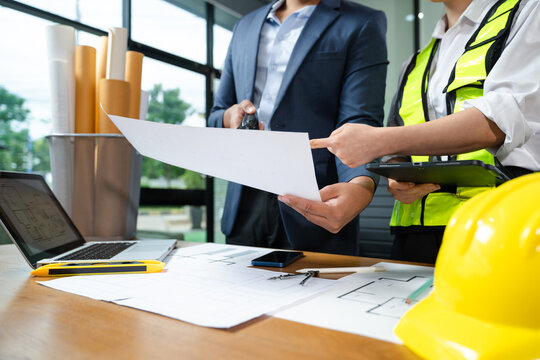 Construction manager and engineer discuss floor plan and project safety with tablet and blueprints. Collaboration, planning