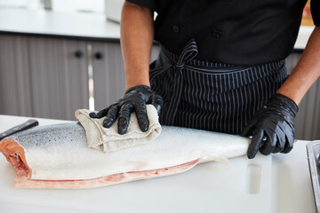closeup chef cleaning raw salmon fish in the kitchen