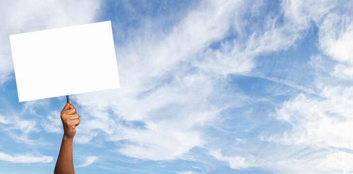 Hand holding a blank sign against a blue sky with fluffy clouds during daylight