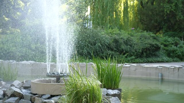 Fountain in a city park. Water splashes upward, shimmering in sunlight. Camera tilts up along the water stream toward the sky. Sunny day, shallow depth of field.