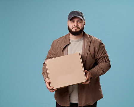 Young man holding a cardboard box in a studio portrait with a blue background