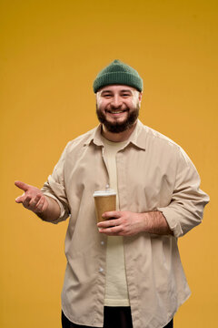 Smiling man in casual clothing holding a coffee cup against a yellow background