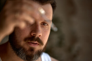 Hybrid skincare. Middle-aged Caucasian man intensely examines a small object under natural light. Concept of meticulous observation and attention to detail.