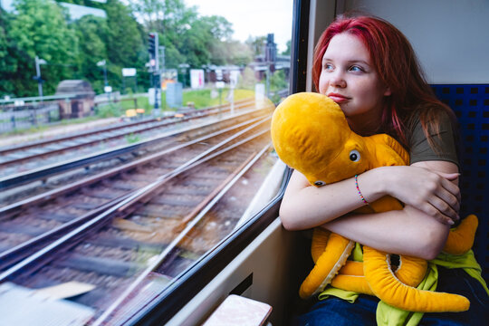 Thoughtful girl with red hair hugging an octopus plush on a train journey.