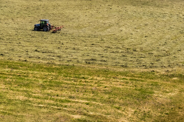 isolated tractor with red attachment mows large field with dry grass in bright daylight. rural agricultural scene
