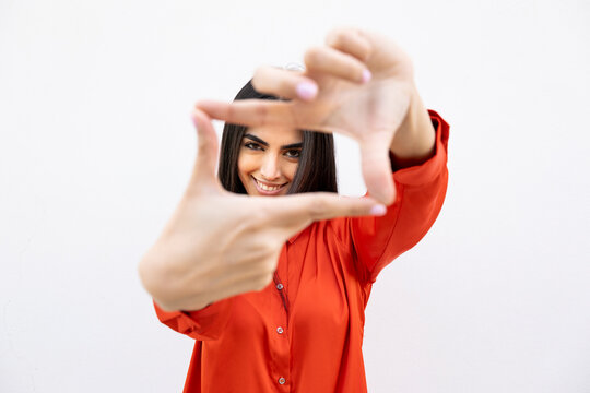 Confident woman in orange shirt framing with hands against white wall