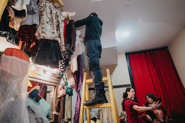 A candid moment of actors organizing and preparing costumes in a backstage setup of a busy theatre.