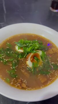Homemade ramen with egg, green onions, and sesame seeds served in a bowl. Concept of Asian cuisine, cozy home cooking, and preparing flavorful comfort food with authentic ingredients