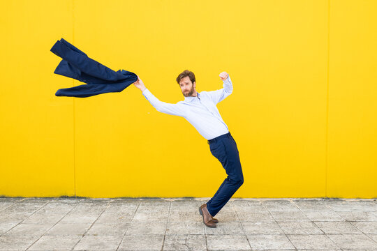 Confident businessman posing with blazer against yellow wall
