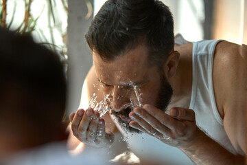 Skin-realism. Man splashes water on his face, droplets glisten on his skin. Concept of daily...