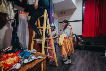 Actors and crew organizing costumes and props in a theater dressing room, getting ready for a...