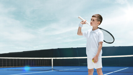 A young boy in a white tennis outfit holds a racket and ball on a blue 3D court under a clear sky....