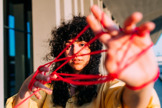 Young woman playing cats cradle with red thread