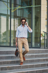 A man dressed in a light blue shirt and beige pants is walking down the steps of a modern office...