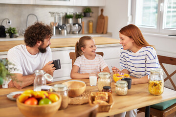 A family of three sits at a wooden table in a modern kitchen, happily sharing breakfast on a weekend morning, filled with laughter and warm conversation over healthy meals.
