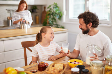 A father and daughter share a joyful moment at the breakfast table, while the mother prepares tea...