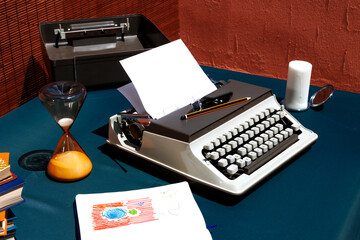 Vintage desk with a mechanical typewriter, hourglass, and candle creating a nostalgic atmosphere