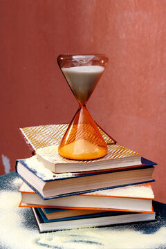 Hourglass on a stack of books with sand spilling over indoors