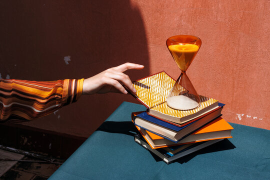 Hand reaching for a book on a stack with an hourglass on a table