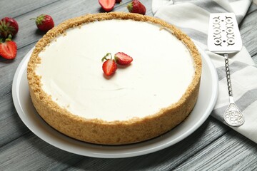 One tasty cheesecake, strawberries and server on grey wooden table, closeup