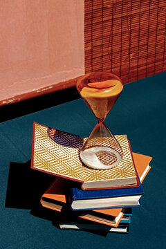 Hourglass on a stack of books with patterned shadows in a conceptual still life