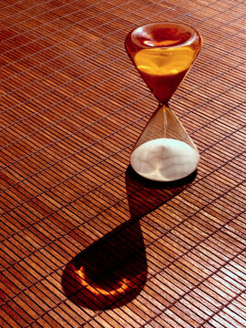 Hourglass casting a shadow on a bamboo mat during golden hour