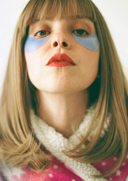 Woman with eye pads and red lipstick looking at camera indoors