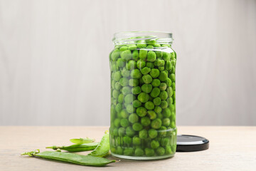 Fresh green peas in pickling jar and pods on wooden table