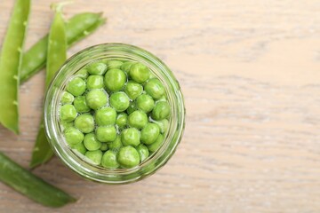 Fresh green peas in pickling jar and pods on wooden table, flat lay. Space for text