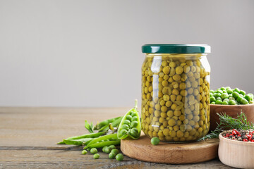 Pickled peas in jar, spices, dill and pods on wooden table, closeup. Space for text
